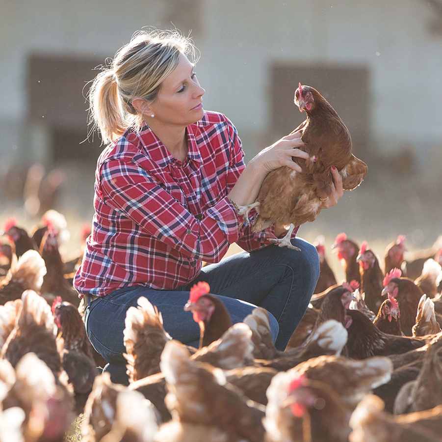 Female farmer surrounded by chickens, holding a chicken